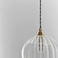Soho Medium Ribbed Glass Shade pendant light with clear ribbed glass and brass fitting suspended by a twisted black cord against a light grey background