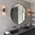 Aldbury Bathroom double wall light with two clear glass shades in matte black finish beside round mirror over double sink vanity