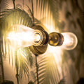 Aldbury Bathroom double wall light with clear glass shades and satin brass finish illuminating palm leaf wallpaper