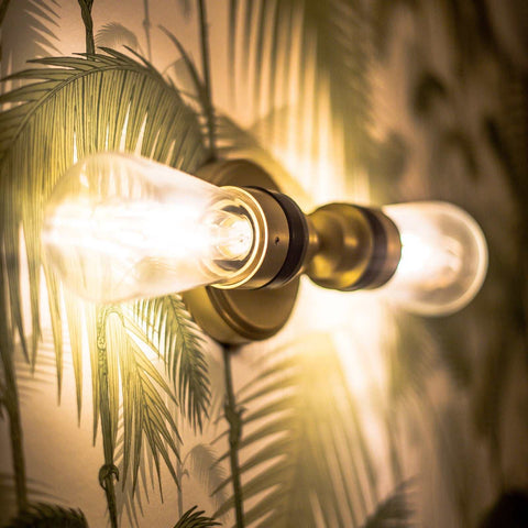Aldbury Bathroom double wall light with clear glass shades and satin brass finish illuminating palm leaf wallpaper