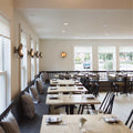 Chulainn Bathroom Dish Wall Light with brass dish shade illuminating a modern dining room with wooden tables and chairs