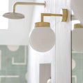 Jordan White Glass Bathroom Wall light fixture with gold arm and white glass shade on a mirror.
