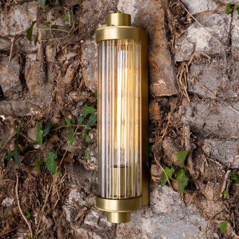 Louise Bathroom Wall Light with elegant reeded glass and brass finish mounted on a rustic stone wall.