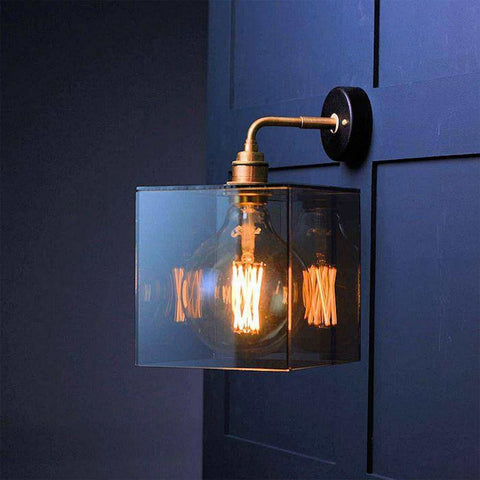Bramley Bathroom smoked glass globe wall light with exposed LED filament bulb and brass arm mounted on dark wall