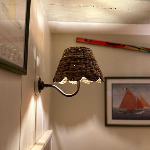 Natural seagrass shade bathroom wall light with swan neck fitting casting warm cozy glow