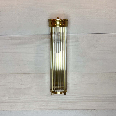 Decorative wall sconce with bright brass finish on a light wooden panel background