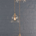Bodium small clear glass shade cluster pendant light with hand-finished metalwork and adjustable flex length against a gray brick wall background