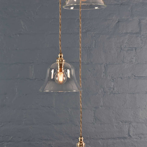 Bodium small clear glass shade cluster pendant light with hand-finished metalwork and adjustable flex length against a gray brick wall background
