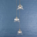Bodium Small Ribbed Glass Shade cluster pendant light with three clear ribbed glass shades hanging against a blue brick wall