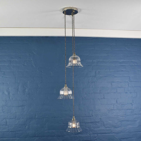 Bodium small ribbed glass shade cluster pendant light with three clear hand-blown glass shades hanging at different lengths against a blue wall