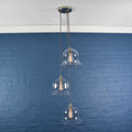 Bodium Large clear glass shade cluster pendant light with three hand-blown bell-shaped shades against blue brick wall