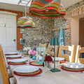 Dining area with a table set for four, colorful pendant lights, and stone walls.