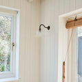 Nook with a wall sconce, window, and yellow flowers on a white paneled wall.