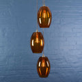 Camber Large amber glass shade cluster pendant light with three oval handmade amber glass shades against a blue brick wall background