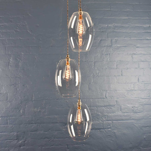 Camber large clear glass shade cluster pendant light with three handmade oval glass shades hanging against a gray brick wall