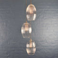 Camber large ribbed glass cluster pendant light with three oval handmade ribbed glass shades hanging against a textured gray wall