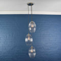 Camber Large Ribbed Glass cluster pendant light with three handmade ribbed oval glass shades hanging against a blue brick wall