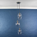 Camber large clear glass shade cluster pendant light with three oval glass shades hanging against a blue brick wall background