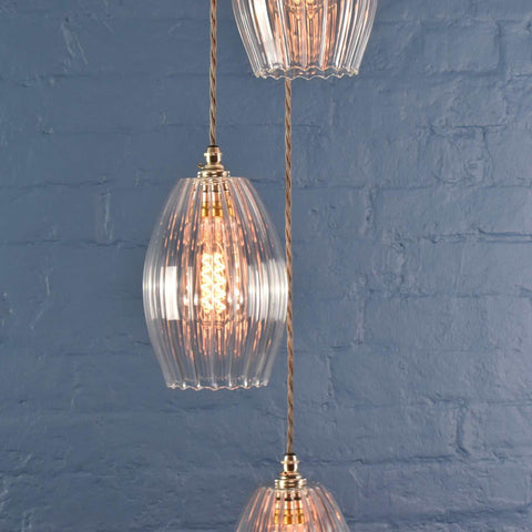 Camber Medium Ribbed Glass Shade cluster pendant light with three elegant oval ribbed glass shades emitting warm vintage-inspired glow against a blue wall background