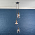 Modern Camber Medium clear glass shade cluster pendant light with three oval shades hanging against a blue brick wall