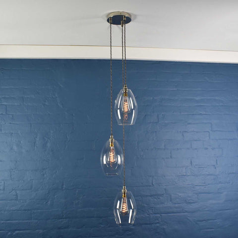 Modern Camber Medium clear glass shade cluster pendant light with three oval shades hanging against a blue brick wall