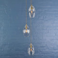 Camber small clear glass shade cluster pendant light with adjustable hanging cords and vintage-style filament bulbs against a blue brick wall background