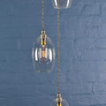 Camber small clear glass shade cluster pendant light with hand-blown glass and adjustable metal fittings against a textured blue brick wall background