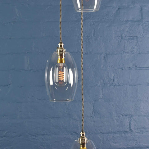 Camber small clear glass shade cluster pendant light with hand-blown glass and adjustable metal fittings against a textured blue brick wall background