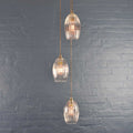 Camber small ribbed glass shade cluster pendant light with hand-blown glass and adjustable cords against a gray brick wall.
