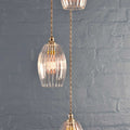 Camber small ribbed glass shade cluster pendant light with vintage design and adjustable brass fittings against a gray brick wall background