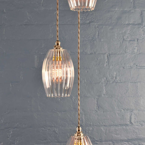 Camber small ribbed glass shade cluster pendant light with vintage design and adjustable brass fittings against a gray brick wall background