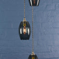Camber small smoked glass shade cluster pendant light with modern design and warm diffused glow hanging against blue brick wall