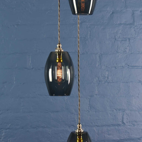 Camber small smoked glass shade cluster pendant light with modern design and warm diffused glow hanging against blue brick wall