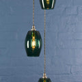 Camber small teal glass shade cluster pendant light with hand-blown glass and adjustable flex hanging against blue brick wall