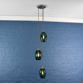 Camber small teal glass shade cluster pendant light with three hand-blown glass shades hanging against a blue brick wall