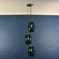 Camber large teal glass cluster pendant light with three handmade teal glass shades hanging against a blue brick wall