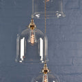 Hythe medium clear glass shade pendant light with hand-blown glass and brass finish against blue brick wall