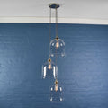 Hythe medium clear glass shade cluster pendant light with three hand-blown glass shades hanging against a blue brick wall