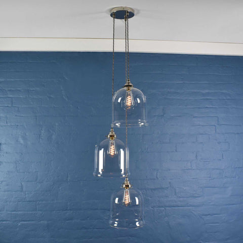 Hythe medium clear glass shade cluster pendant light with three hand-blown glass shades hanging against a blue brick wall