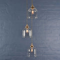 Hythe Small clear glass shade cluster pendant light with handblown bell-shaped shades against a blue brick wall