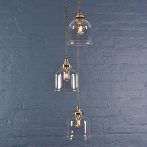 Hythe Small clear glass shade cluster pendant light with handblown bell-shaped shades against a blue brick wall