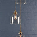 Hythe Small Clear Glass Shade cluster pendant light with handblown bell-shaped shades and brass fittings against a blue brick wall