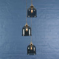 Hythe small smoked glass shade cluster pendant light with three hand-blown smoked glass cloche shades hanging against blue brick wall