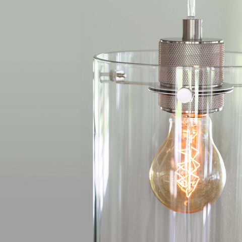Dunsford Cylindrical Pendant Light with clear glass shade and metal finish illuminating vintage bulb
