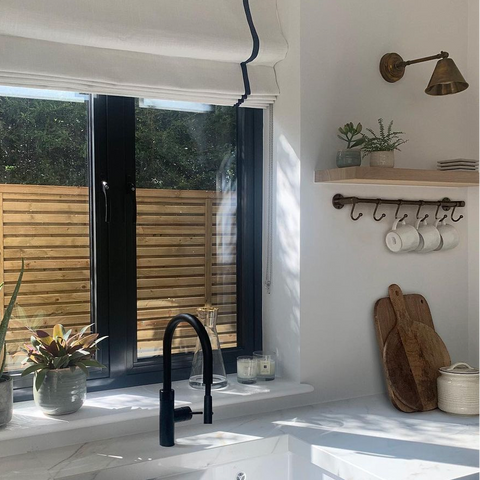 Modern kitchen with a sink, black faucet, and window view of greenery. and henly adjustable brass light.