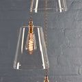 Newbury large tapered glass shade cluster pendant light with exposed filament bulb and braided cord against grey brick wall background
