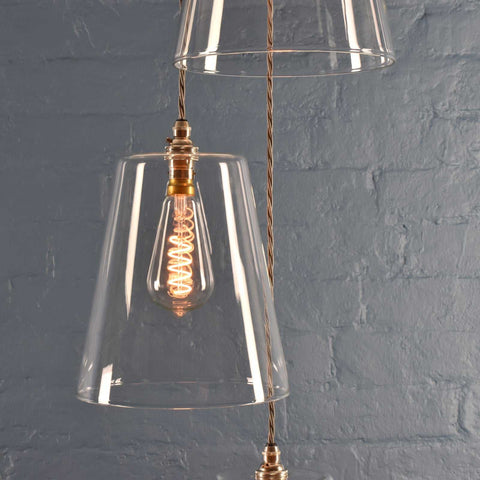 Newbury large tapered glass shade cluster pendant light with exposed filament bulb and braided cord against grey brick wall background