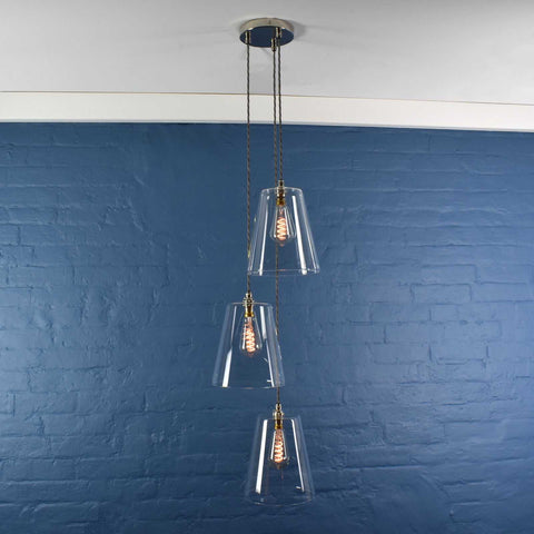 Newbury large tapered glass shade cluster pendant light with three clear glass shades and exposed filament bulbs against a blue brick wall background