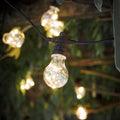 String of outdoor lights with clear glass bulbs hanging against a blurred natural background