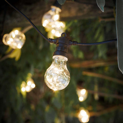 String of outdoor lights with clear glass bulbs hanging against a blurred natural background